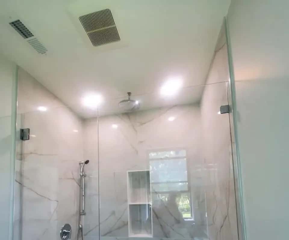 Walk-in shower with large marble-look wall tile, a frameless glass panel, a built-in niche and a window