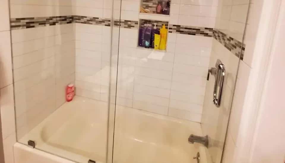 Bathtub with a fixed glass panel, white subway tile, a mosaic accent band and a tiled niche