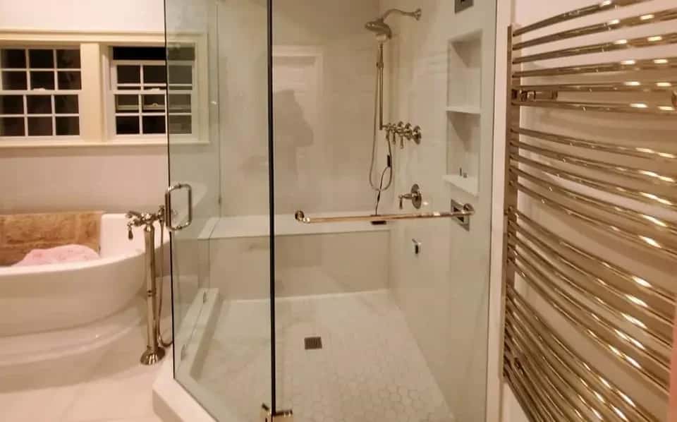 Corner glass shower with brass fixtures next to a freestanding tub and a brass towel warmer
