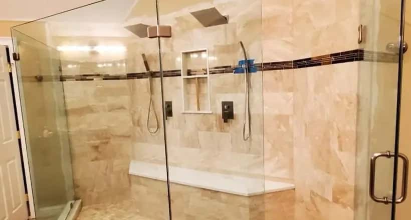 Neo-angle glass shower in beige stone-look tile with a built-in bench, a recessed niche and a mosaic accent band