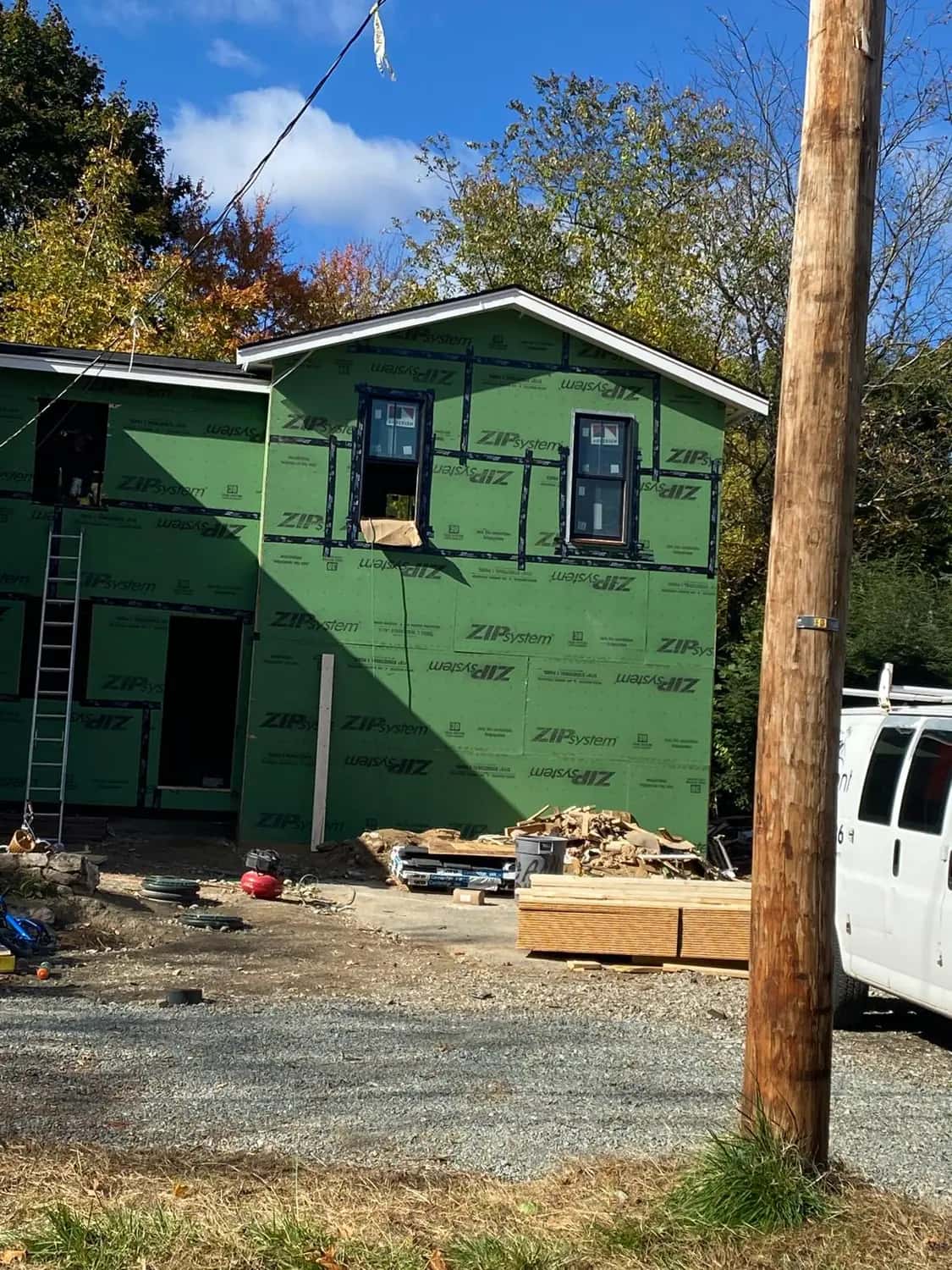 Two-story addition in taped green sheathing with its windows installed, seen from the driveway