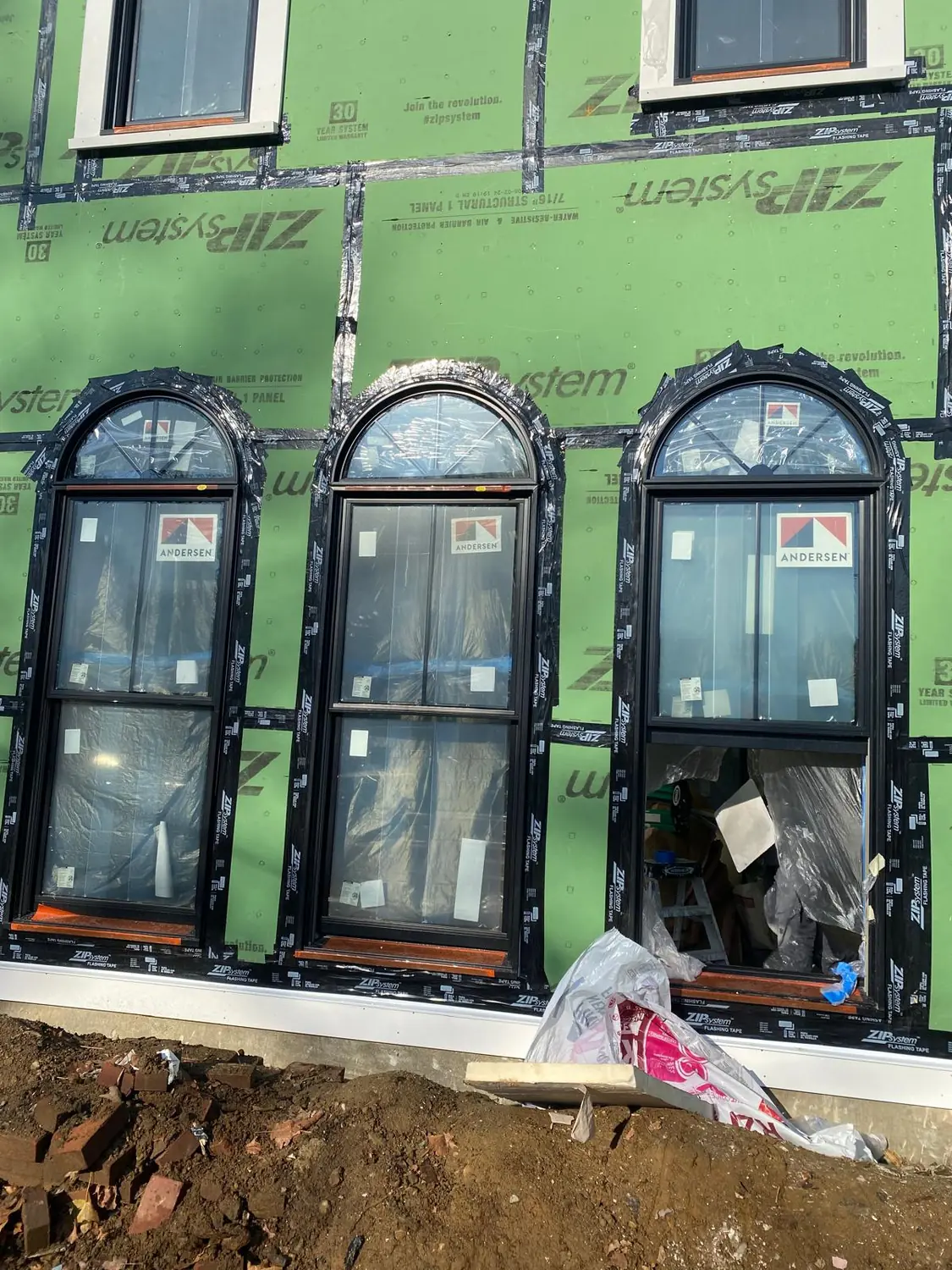 Three new arched windows with factory labels still on, set into green sheathing with taped seams, Lynnfield, MA