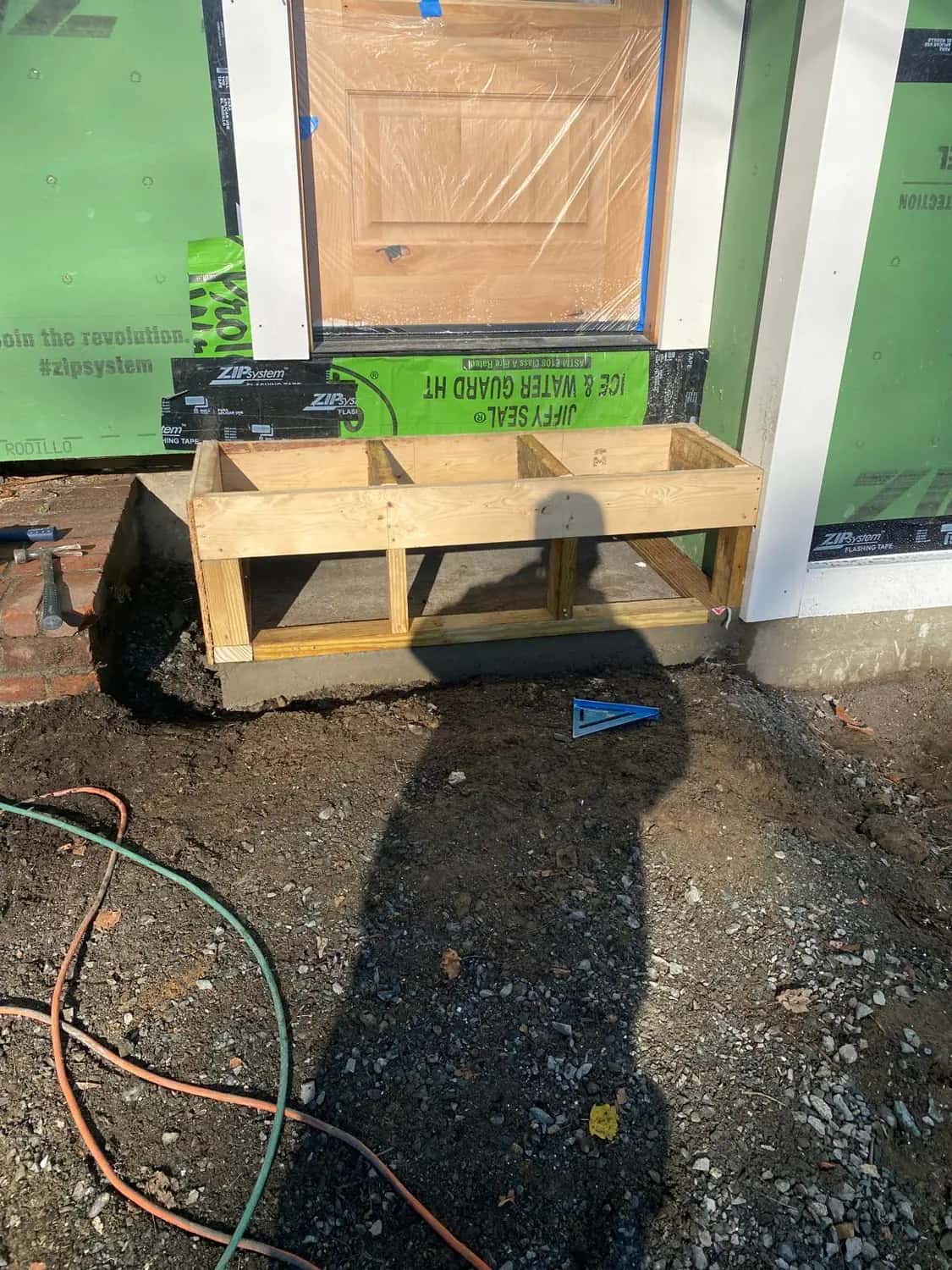 New entry door in protective plastic, with flashing membrane at the sill and a wood form for its step, on a home addition in Lynnfield, MA