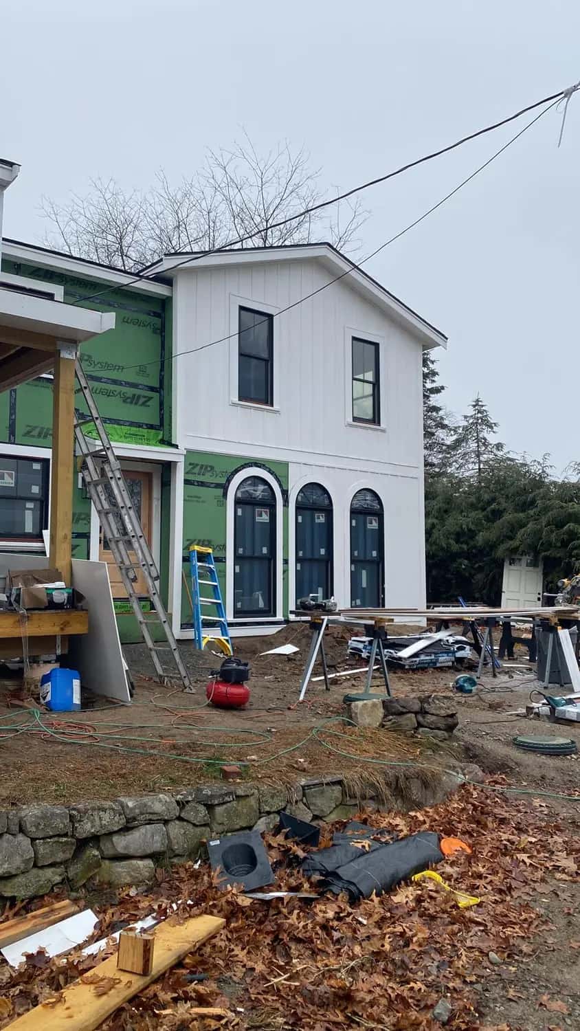 White vertical siding installed on a two-story addition, with a ladder and three arched-top black windows
