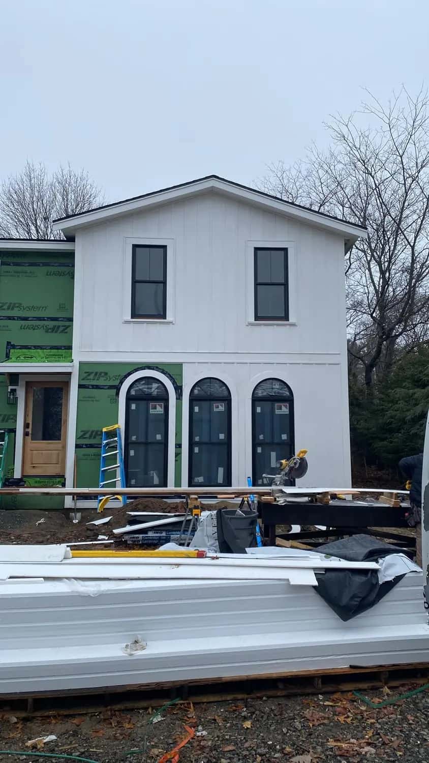 White vertical siding nearly finished around three arched windows and a new entry door on a home addition