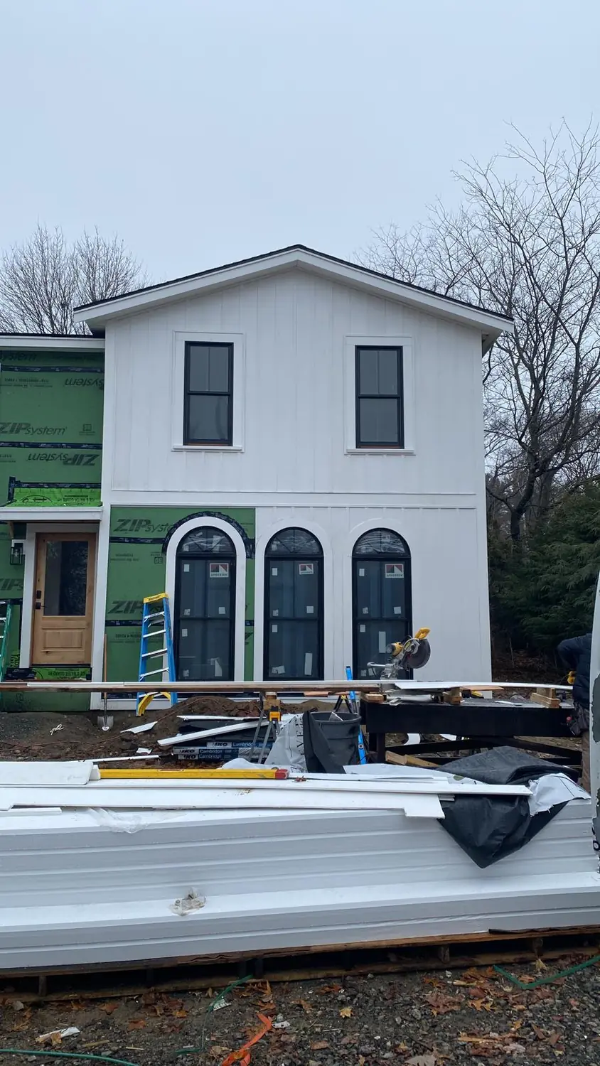 White vertical siding nearly finished around three arched windows and a new entry door on a home addition in Lynnfield, MA