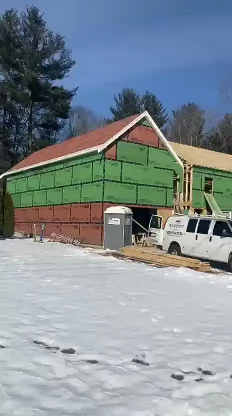 Addition walls sheathed in green and red panels in winter, with a work van parked beside it (video still)