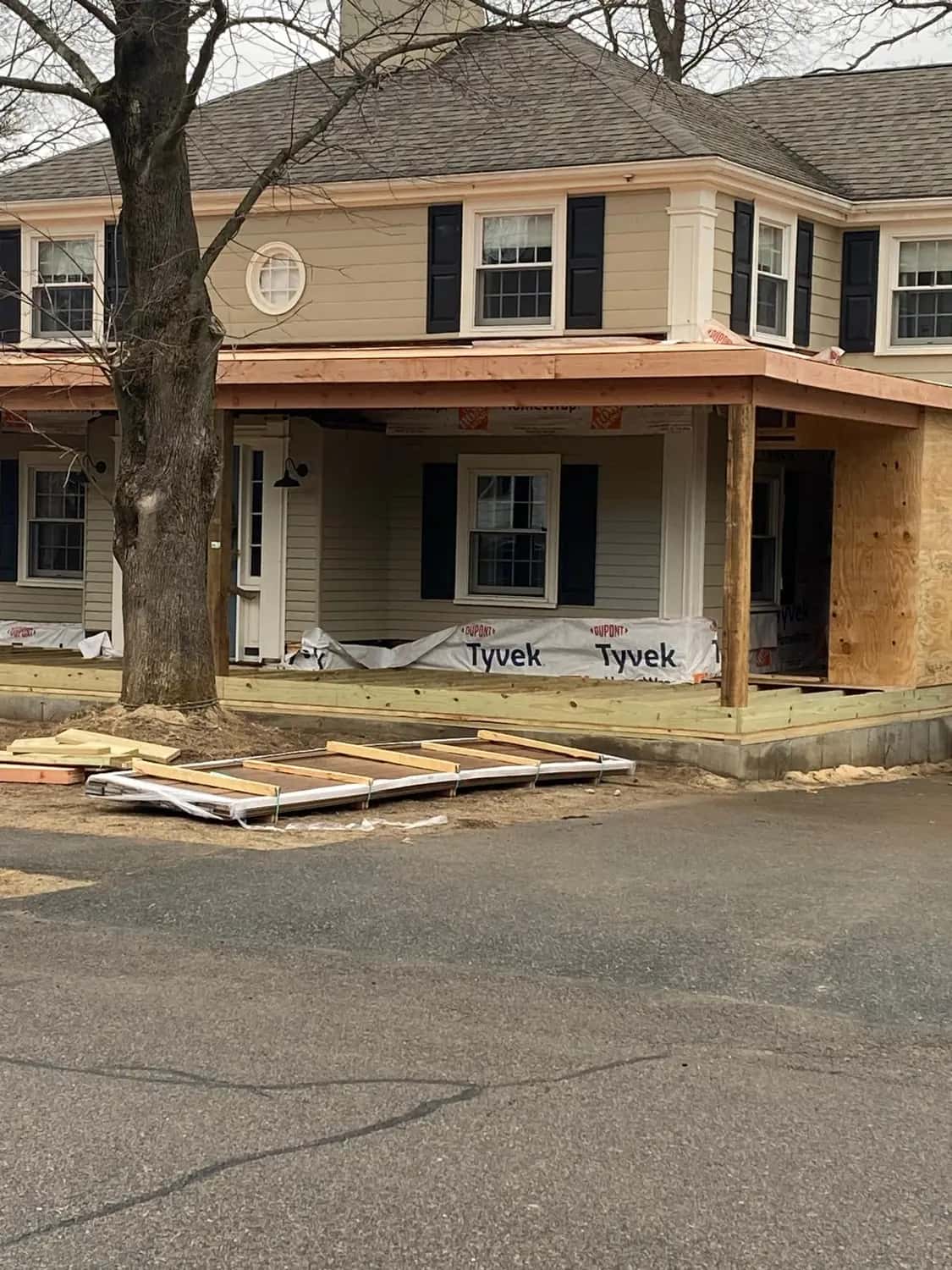 Colonial house with a new front porch roof frame, house wrap along the base and a plywood-sheathed section at the side