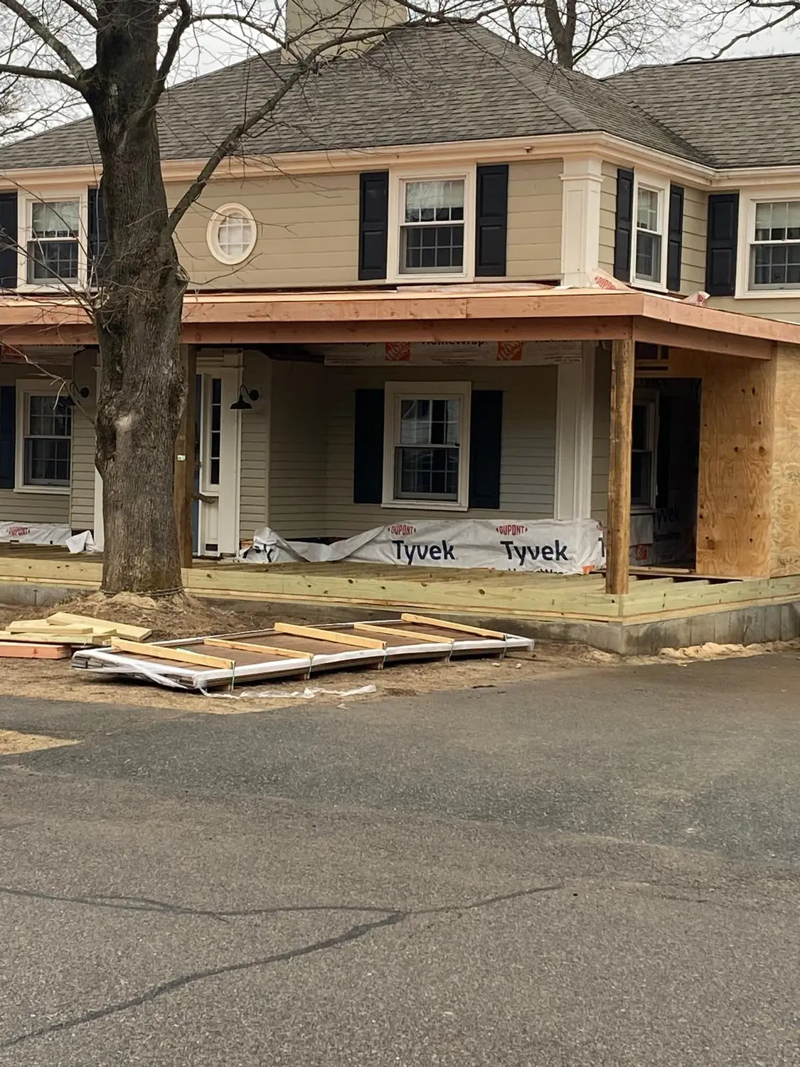 Colonial house in Needham, MA with a new front porch roof frame, house wrap along the base and a plywood-sheathed section at the side