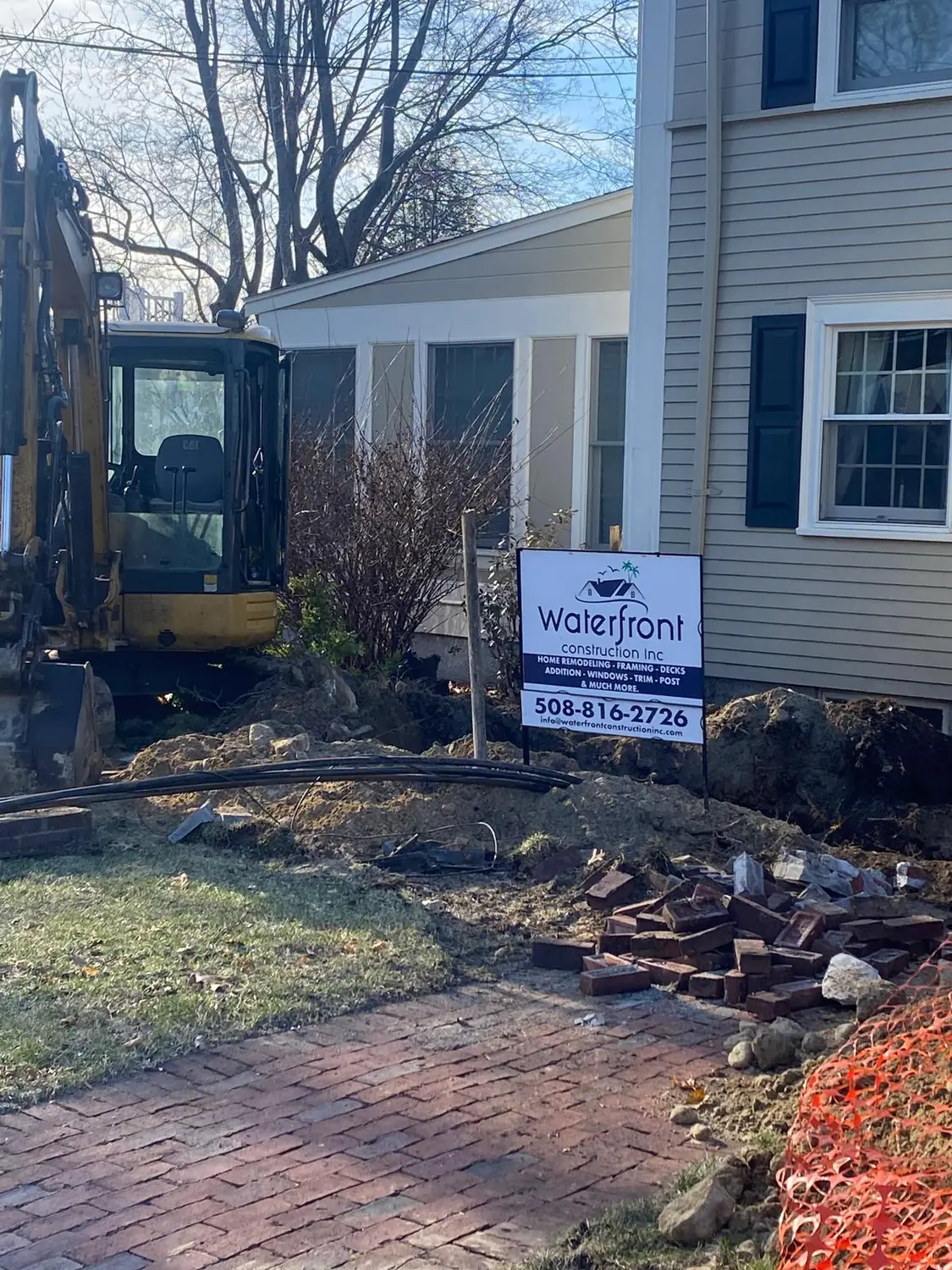 Mini excavator digging beside a colonial house in Needham, MA, next to a Waterfront Construction job sign