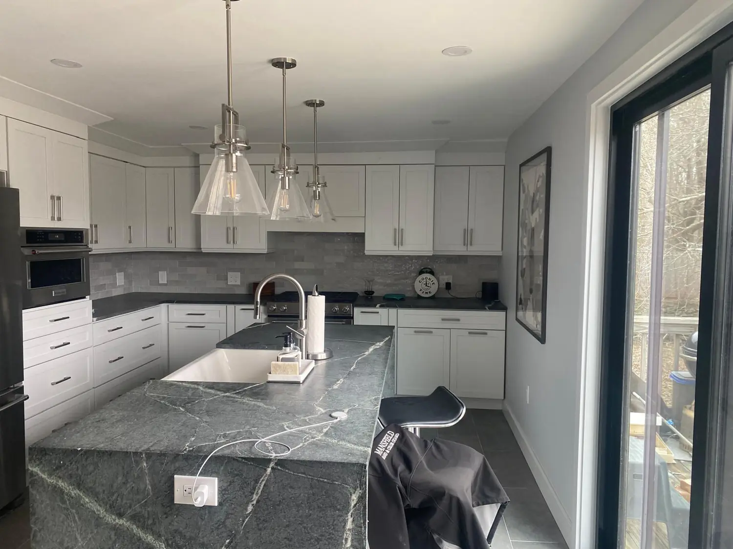 Kitchen island with a dark veined stone-look countertop and waterfall edge, white cabinets and a sliding door